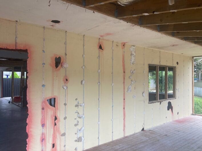 Interior wall studs exposed after asbestos sheeting removal, edges sealed with PVA